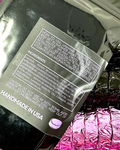 Shower steamers with a label detailing usage and ingredients, set against a reflective surface.