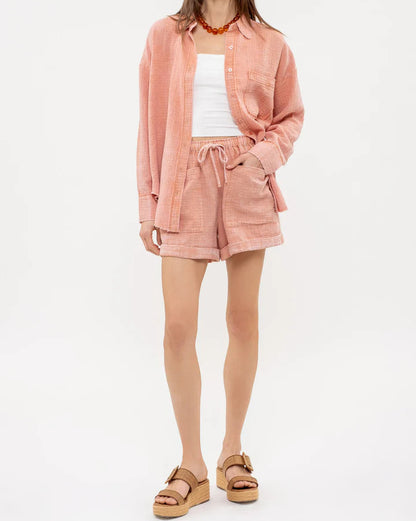 Woman wearing a sienna pink textured button up and matching shorts on a white background.
