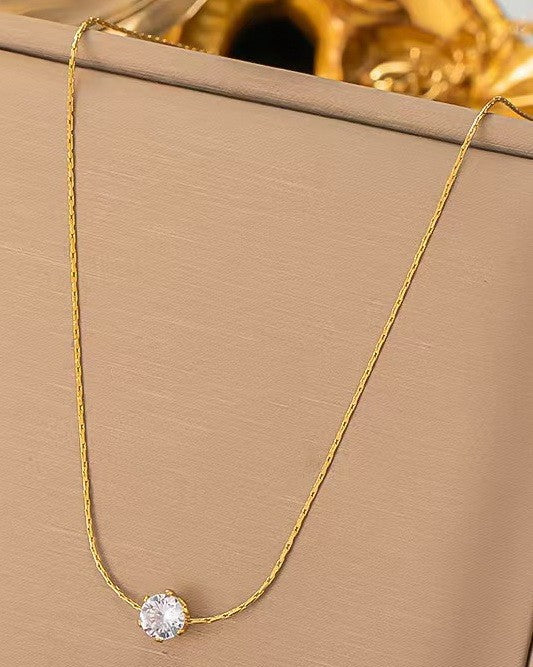 Gold necklace with a diamond pendant on a beige surface