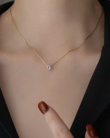Gold necklace with a diamond pendant on a person's neck, with a hand pointing to it.