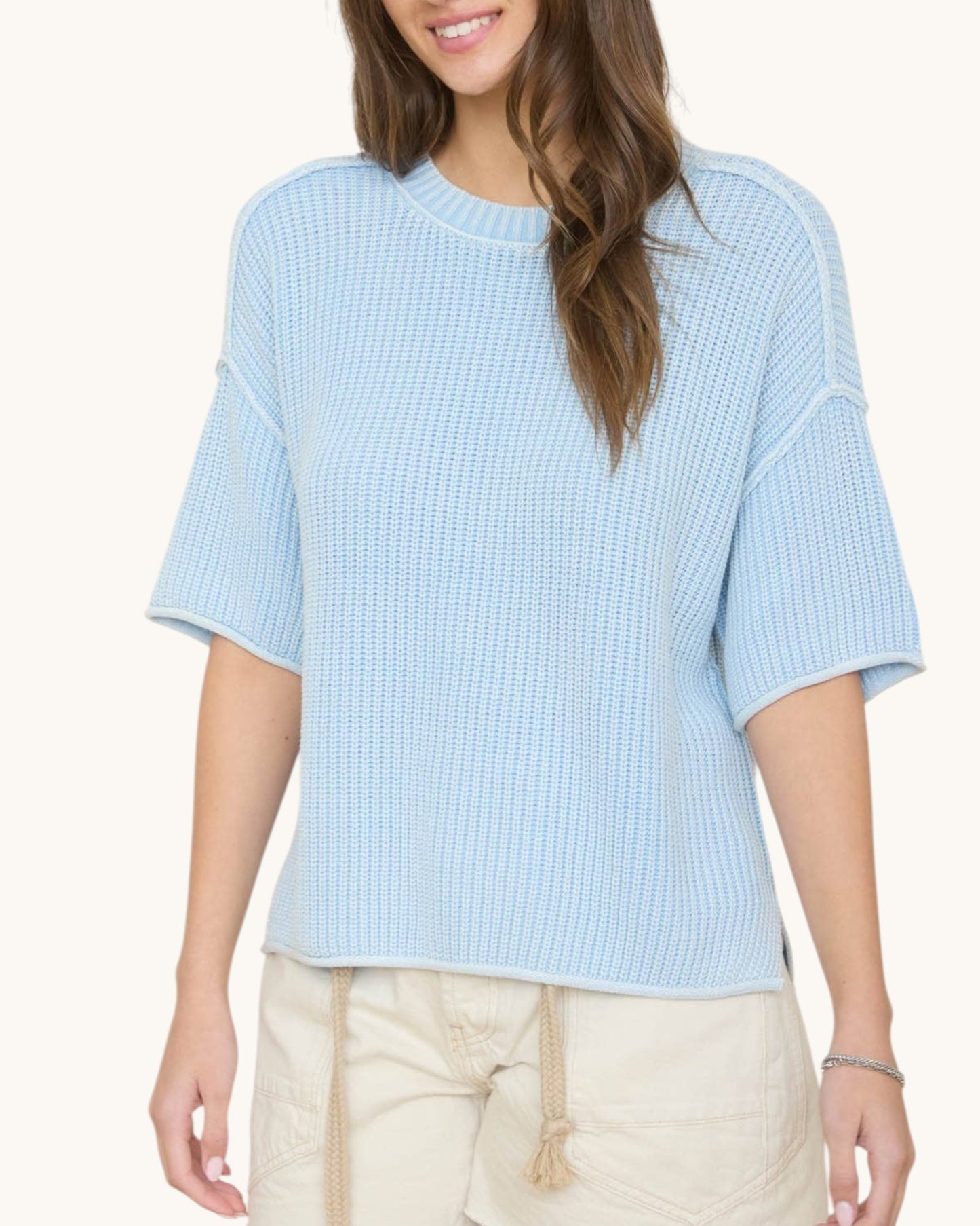 Woman wearing a light blue textured top with beige pants on a white background.