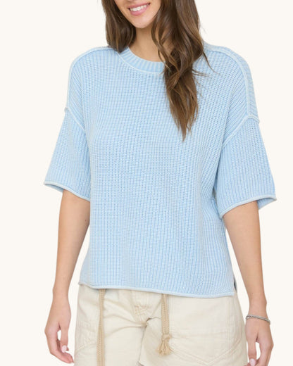 Woman wearing a light blue textured top with beige pants on a white background.