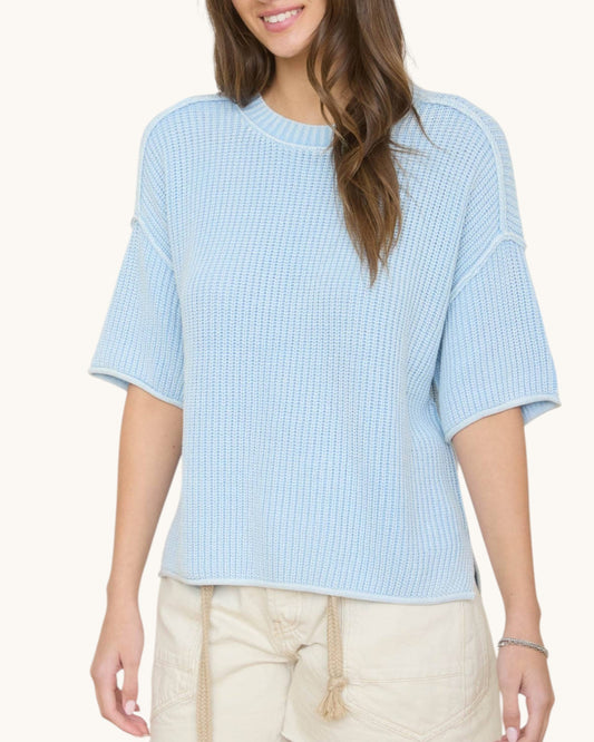 Woman wearing a light blue textured top with beige pants on a white background.