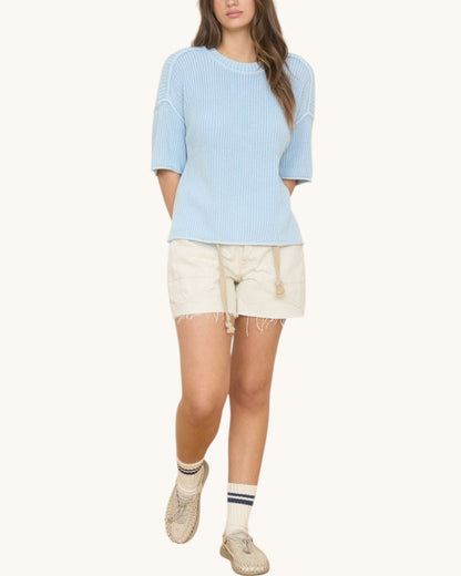 Woman wearing a light blue sweater and white shorts on a white background.