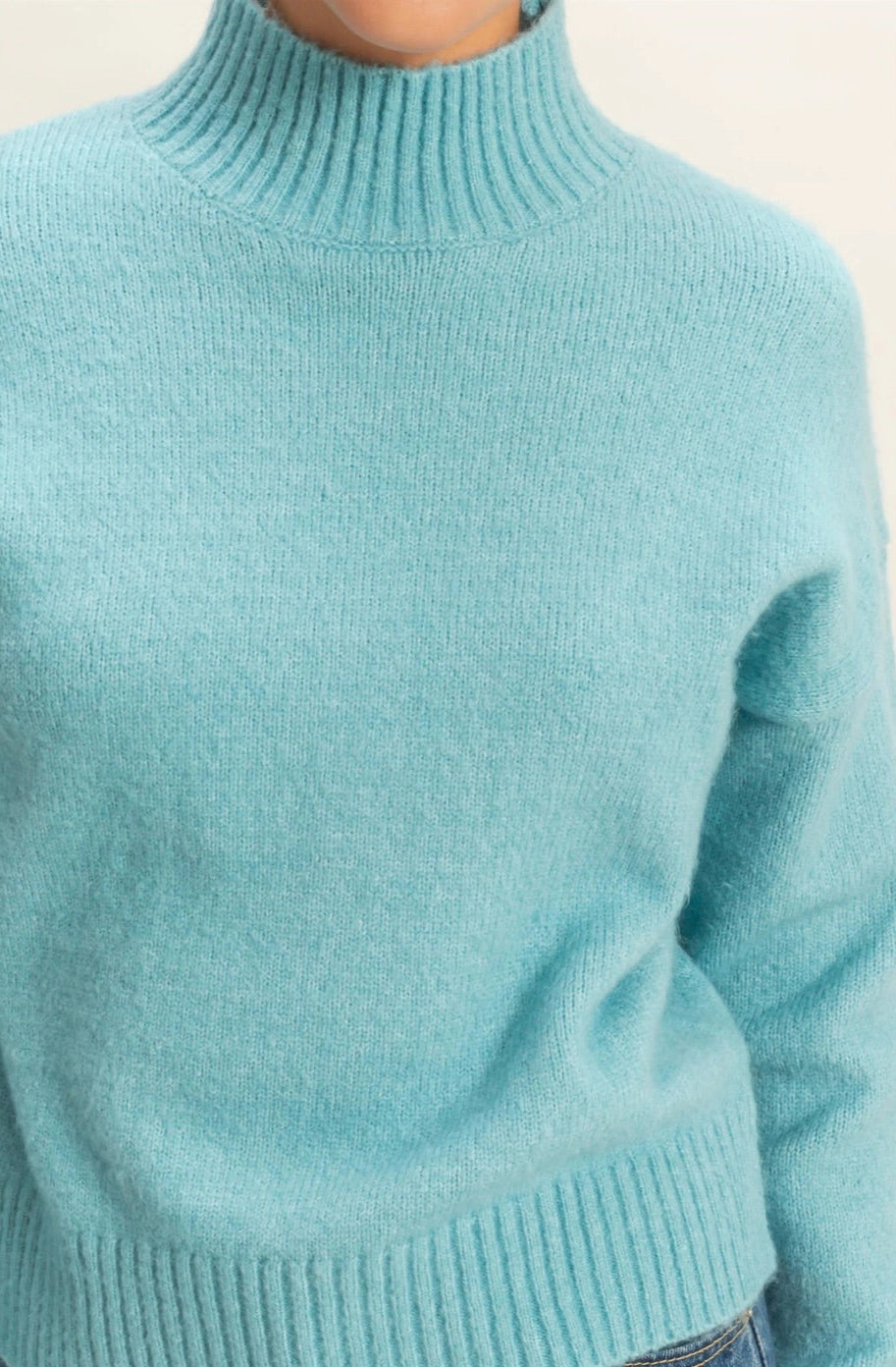 Teal sweater worn by a person on a light beige background.