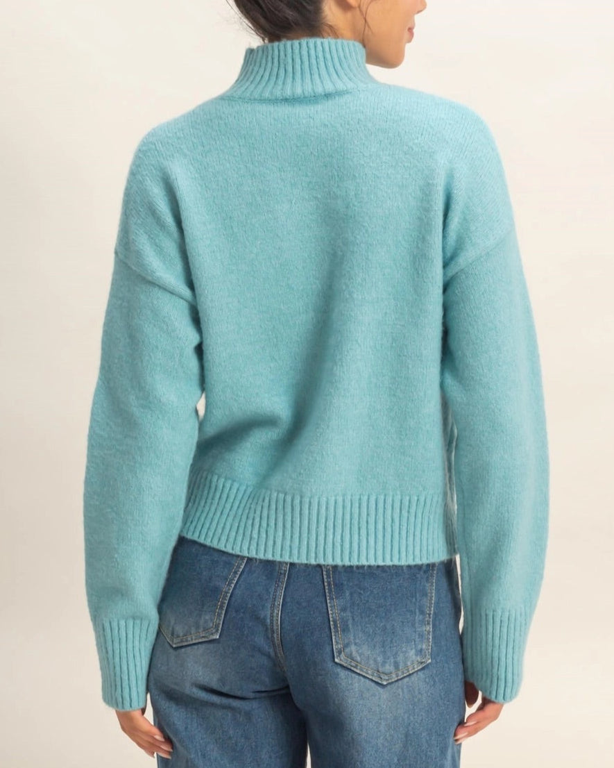 Person wearing a light blue sweater and jeans on a plain background.