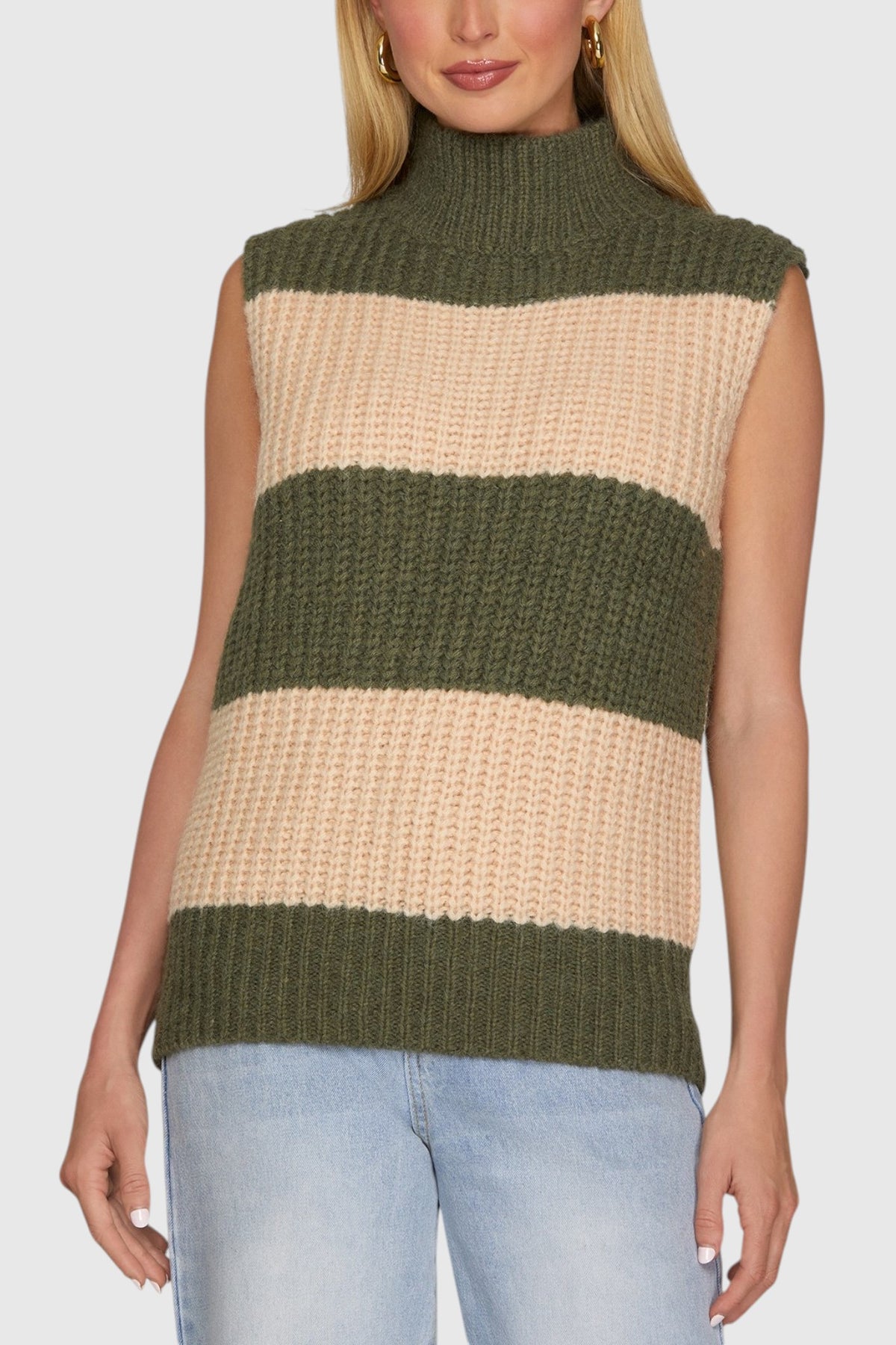 Woman wearing a sleeveless chunky knit sweater with mock neck in Olive and Beige stripes. 