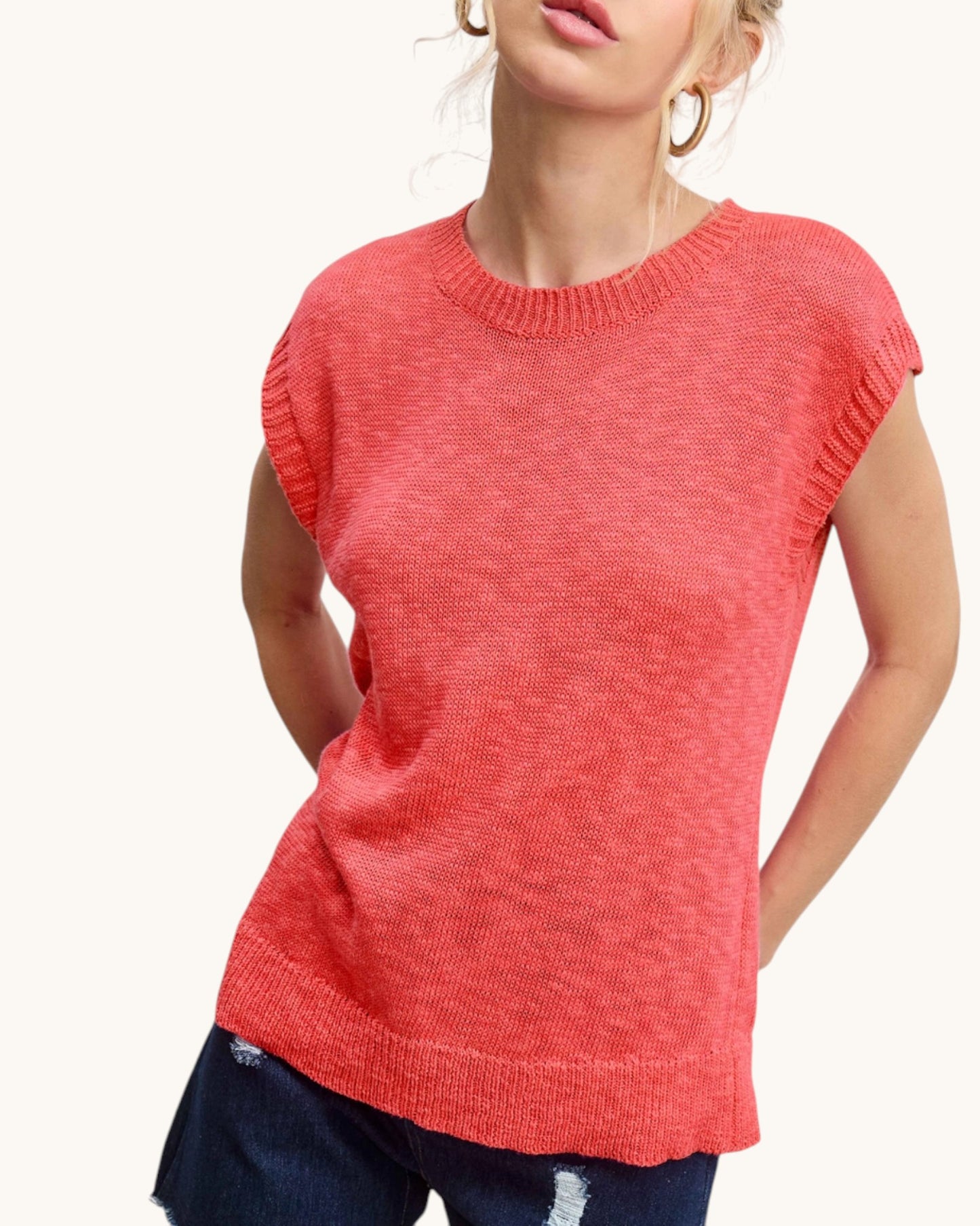 Person wearing a coral sleeveless sweater on a white background.