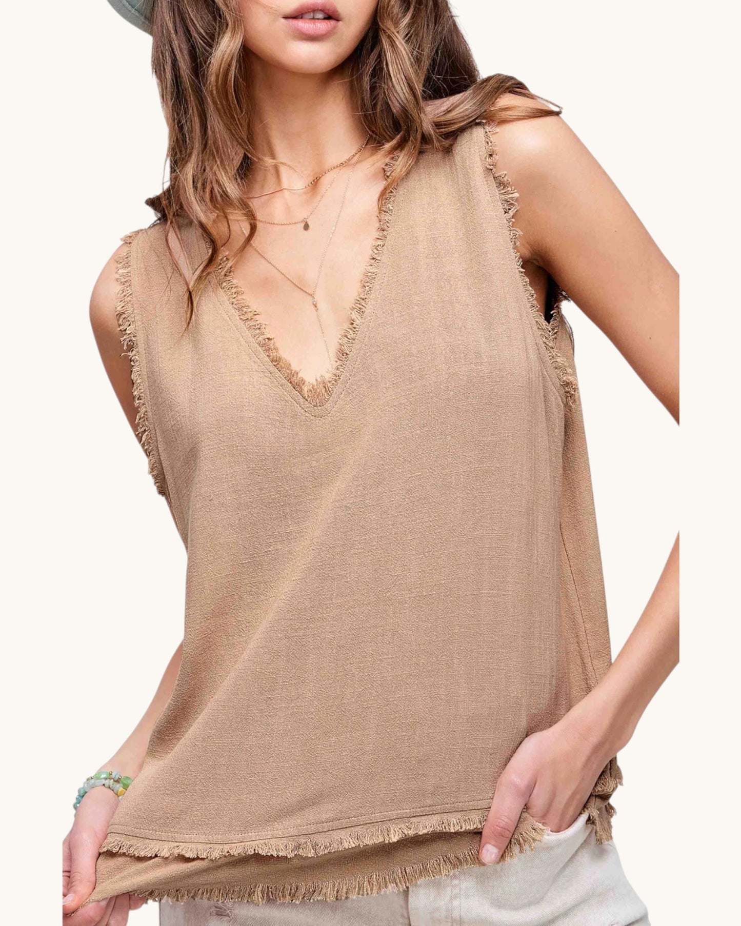 Woman wearing a beige sleeveless top with fringe details on a white background.