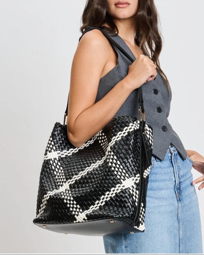 Woman holding a black and white plaid woven vegan leather handbag against a plain background.