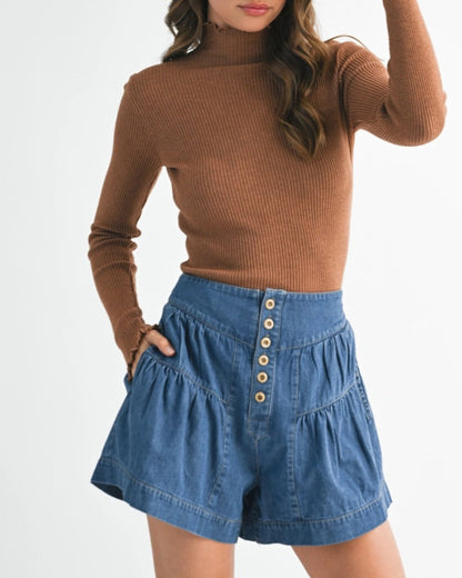 Woman wearing a brown sweater and blue denim shorts on a white background