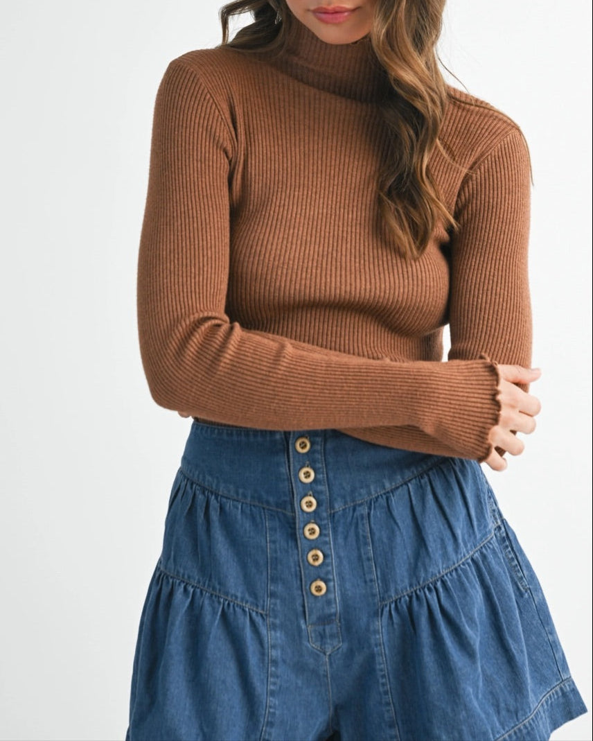 Woman wearing a brown ribbed sweater and blue denim skirt with a white hat on a white background.