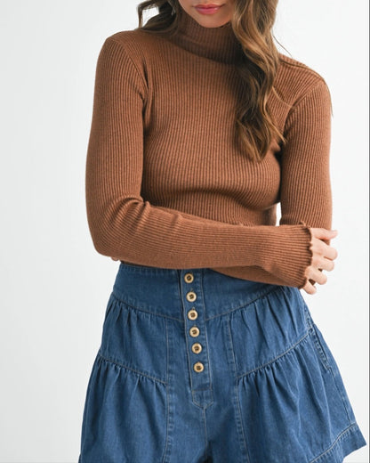 Woman wearing a brown ribbed sweater and blue denim skirt with a white hat on a white background.
