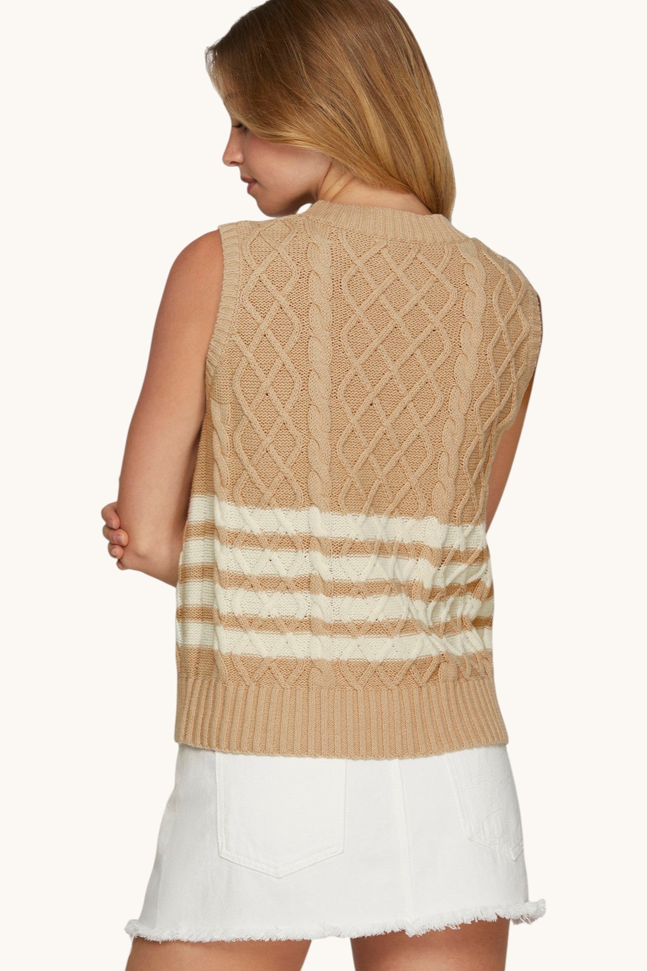 Back view of a woman wearing a sleeveless tan cable knit sweater with white stripes.