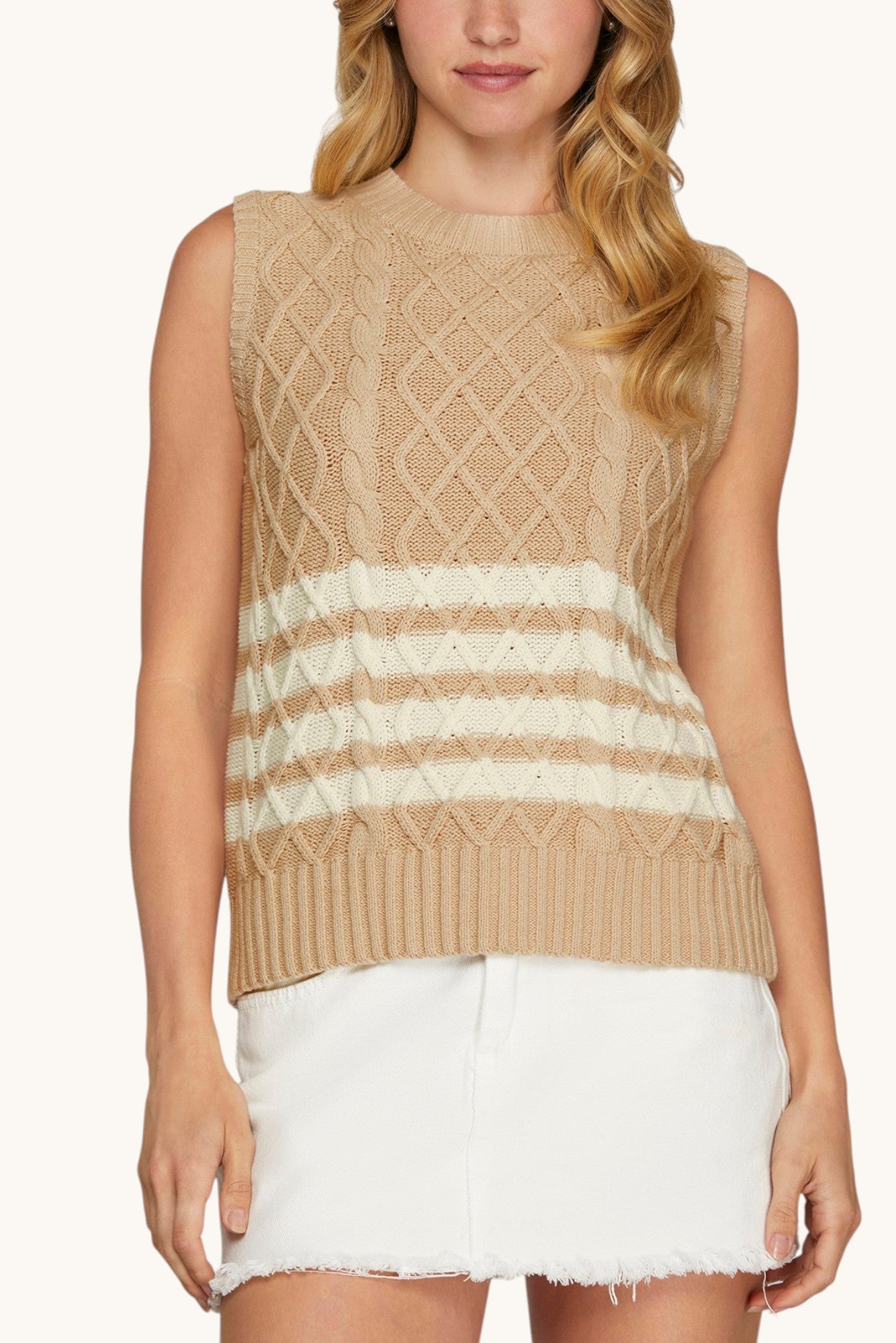 Woman wearing a tan cable knit sleeveless sweater with white stripes on bottom half.