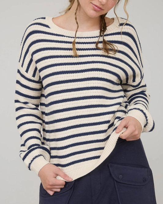 Woman wearing a navy and white striped long sleeve sweater with navy pants against a plain background.