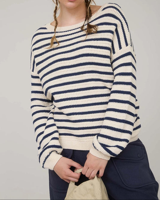 Woman wearing a navy and white striped long sleeve sweater with navy pants against a plain background. 