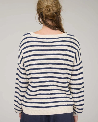 Rear view of a woman wearing a navy and white striped long sleeve sweater with navy pants against a plain background.