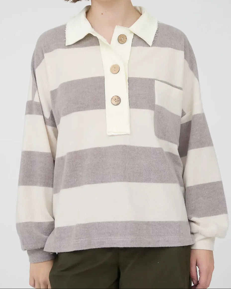 Person wearing a gray and white striped rugby shirt with oversized buttons on a plain background.