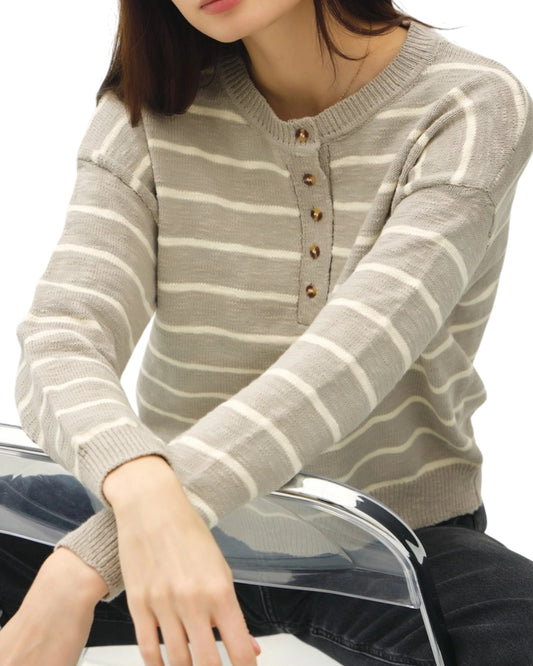 Person wearing a gray and white striped sweater with buttons on a white background.