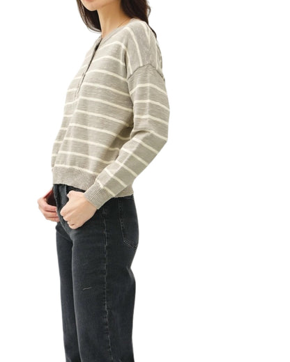 Person wearing a grey striped sweater and dark jeans on a white background.