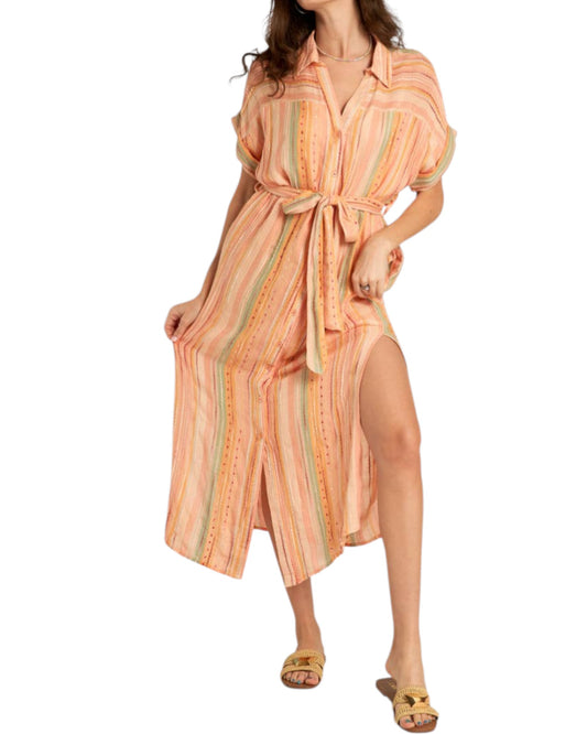 Woman wearing a pinky peach-colored striped midi dress with a slit on a white background.