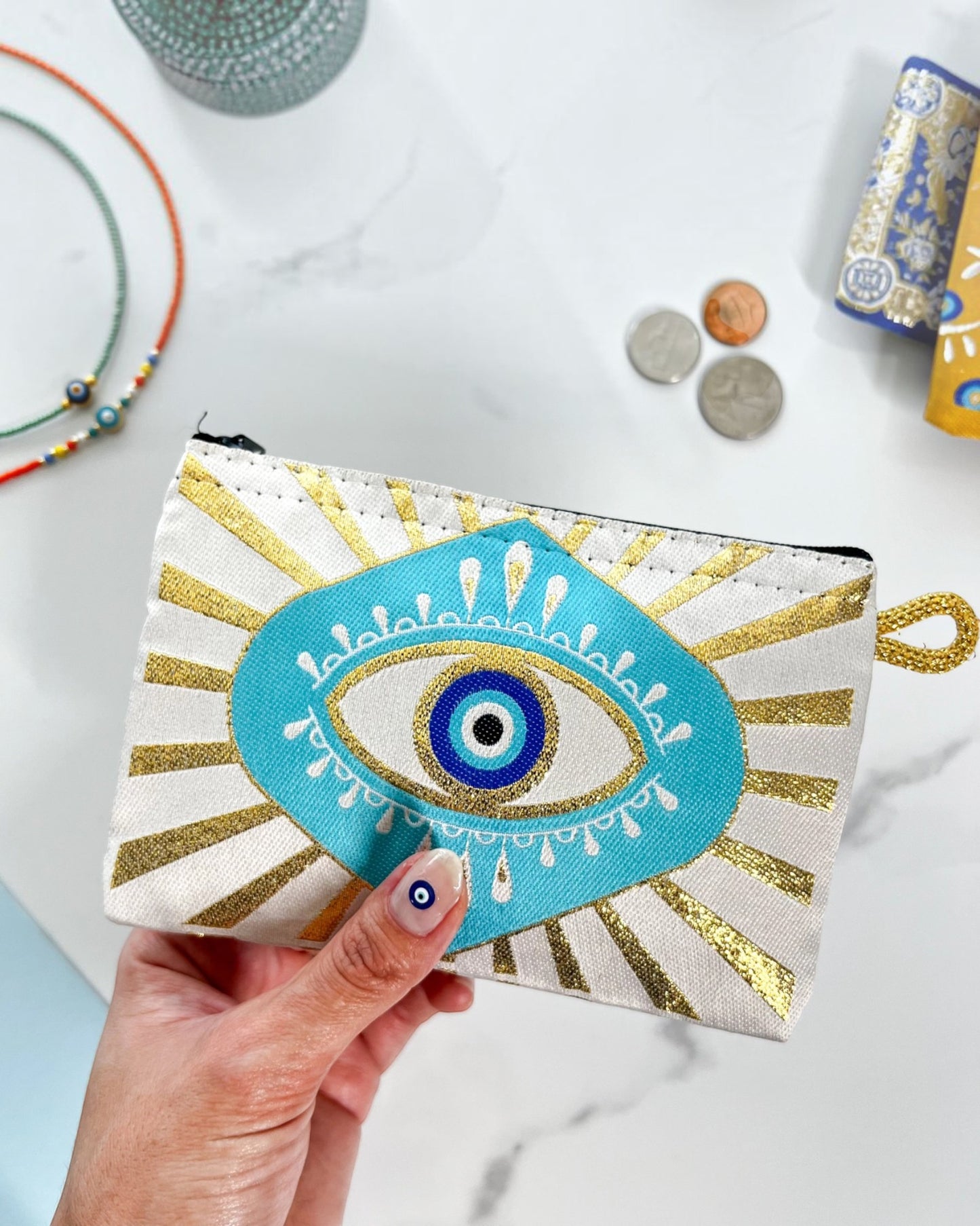 Hand holding a small zipper pouch/coin purse with an eye design against a marble background.