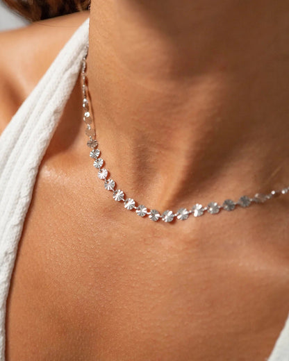 Close-up of a silver sunburst necklace on a person wearing a white top.