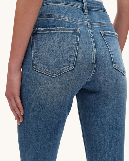 Close-up back view of a person wearing medium-wash blue denim jeans, showing the rear pockets and waistband against a plain light background.