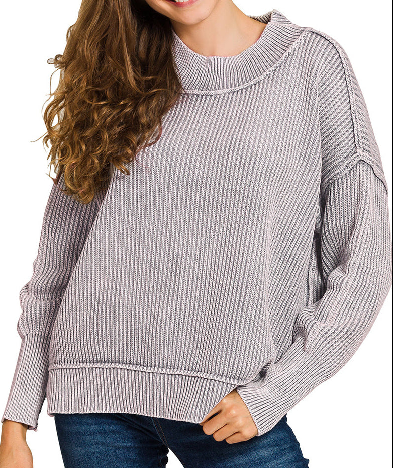 Woman wearing a gray ribbed sweater with a plain background.