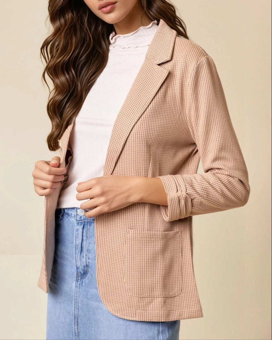 Woman wearing a tan blazer over a white top and blue jeans on a beige background.