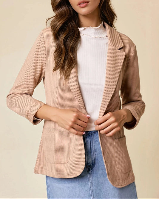 Woman wearing a tan blazer over a white top and blue jeans on a beige background.