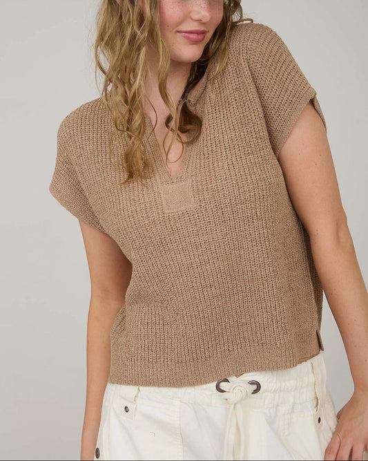 Woman wearing a tan knit top and cap against a plain background