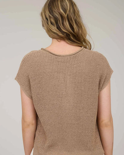 Woman wearing a tan knitted top against a plain background.