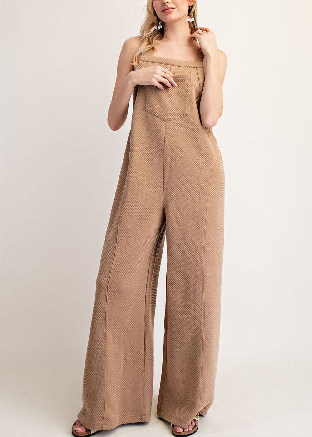 A woman modeling a an wide-leg jumpsuit with a textured pattern, photographed against a plain light gray studio background.