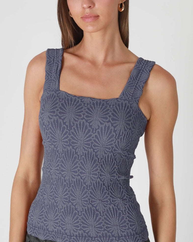 Woman wearing a floral patterned blue tank top on a white background.