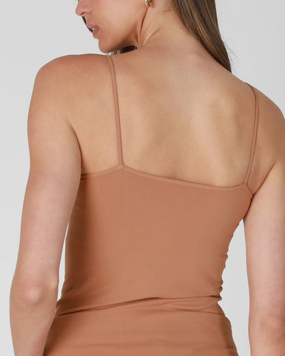 Woman wearing a mocha tank top with thin straps on a plain background.