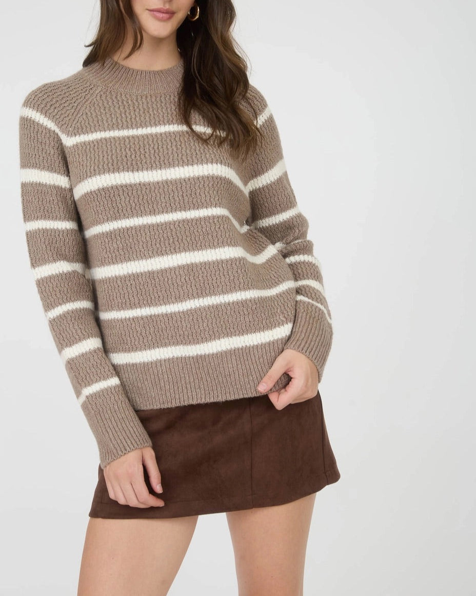 Woman wearing a taupe and ivory striped mock neck sweater with a brown skirt on a white background.