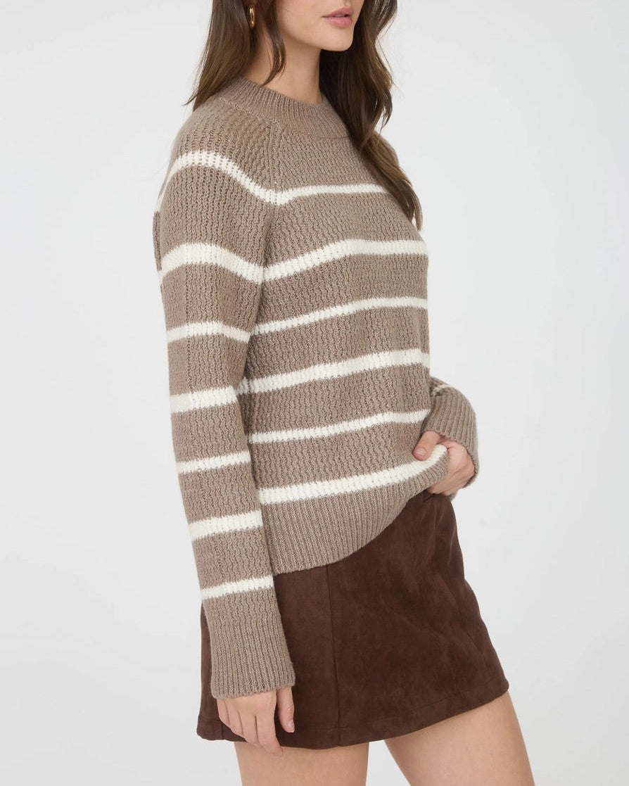 Woman wearing a taupe and ivory striped mock neck sweater with a brown skirt on a white background.