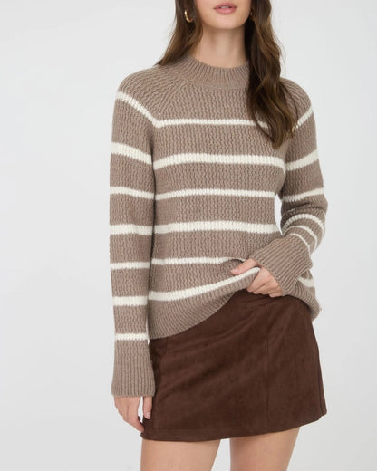 Woman wearing a taupe and ivory striped mock neck sweater with a brown skirt on a white background.