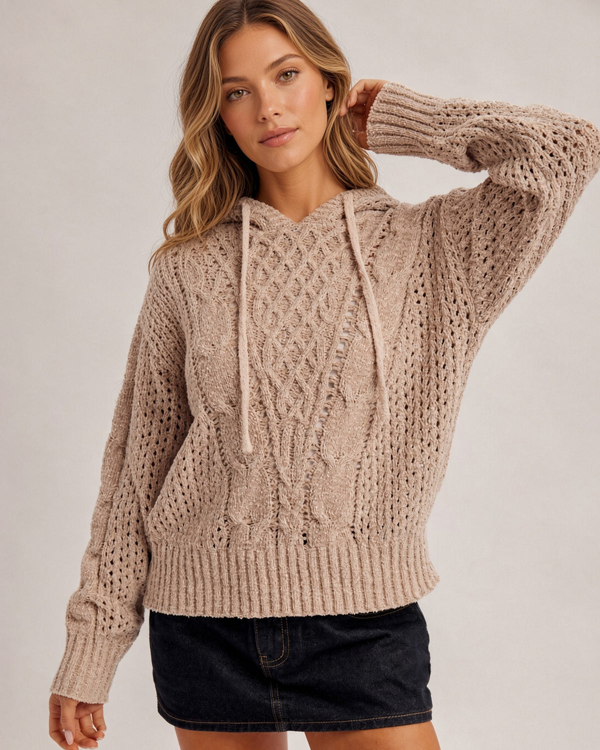 Woman wearing a speckled taupe stretchy hoodie sweater and black denim skirt.