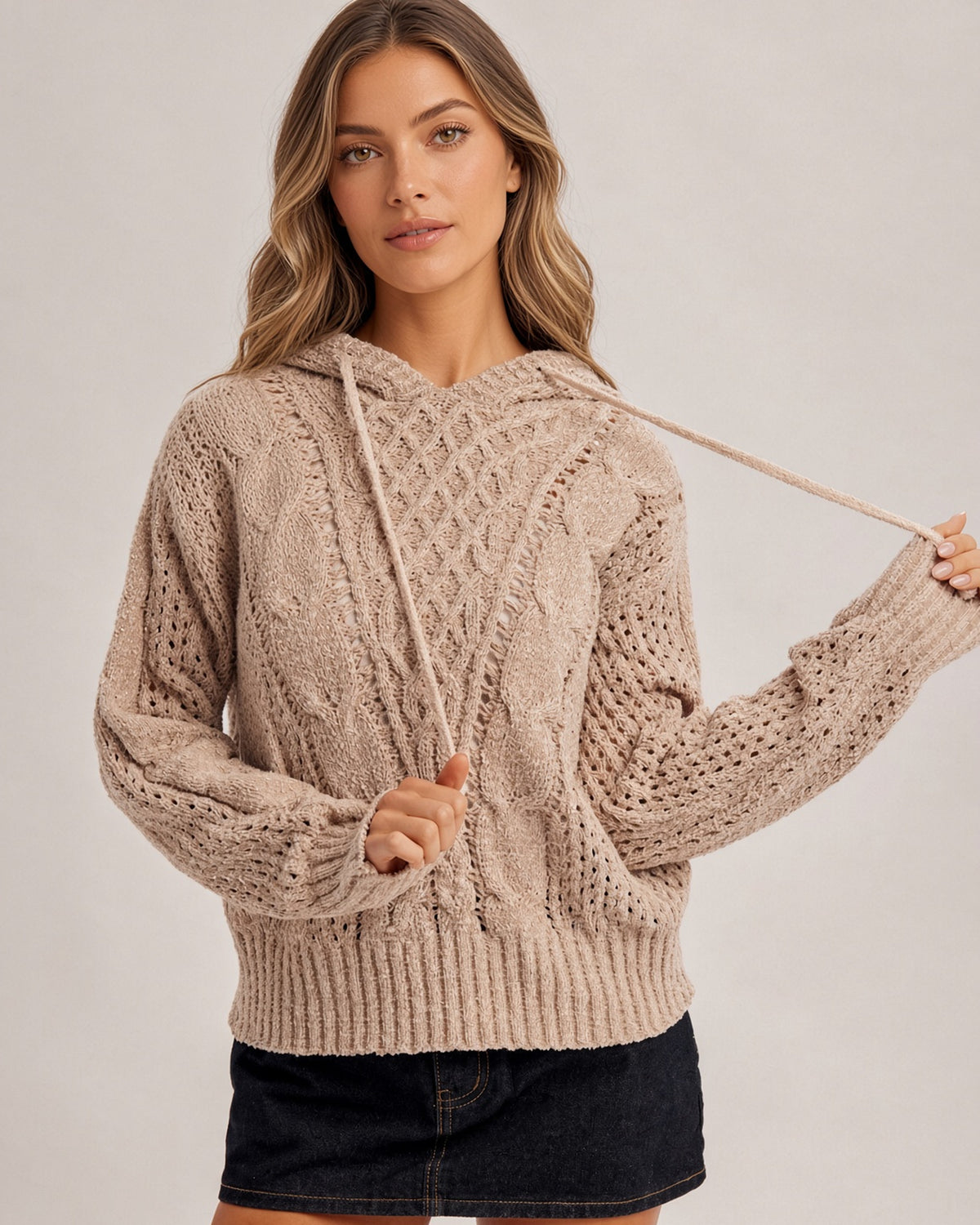 Woman wearing a speckled taupe stretchy hoodie sweater and black denim skirt.