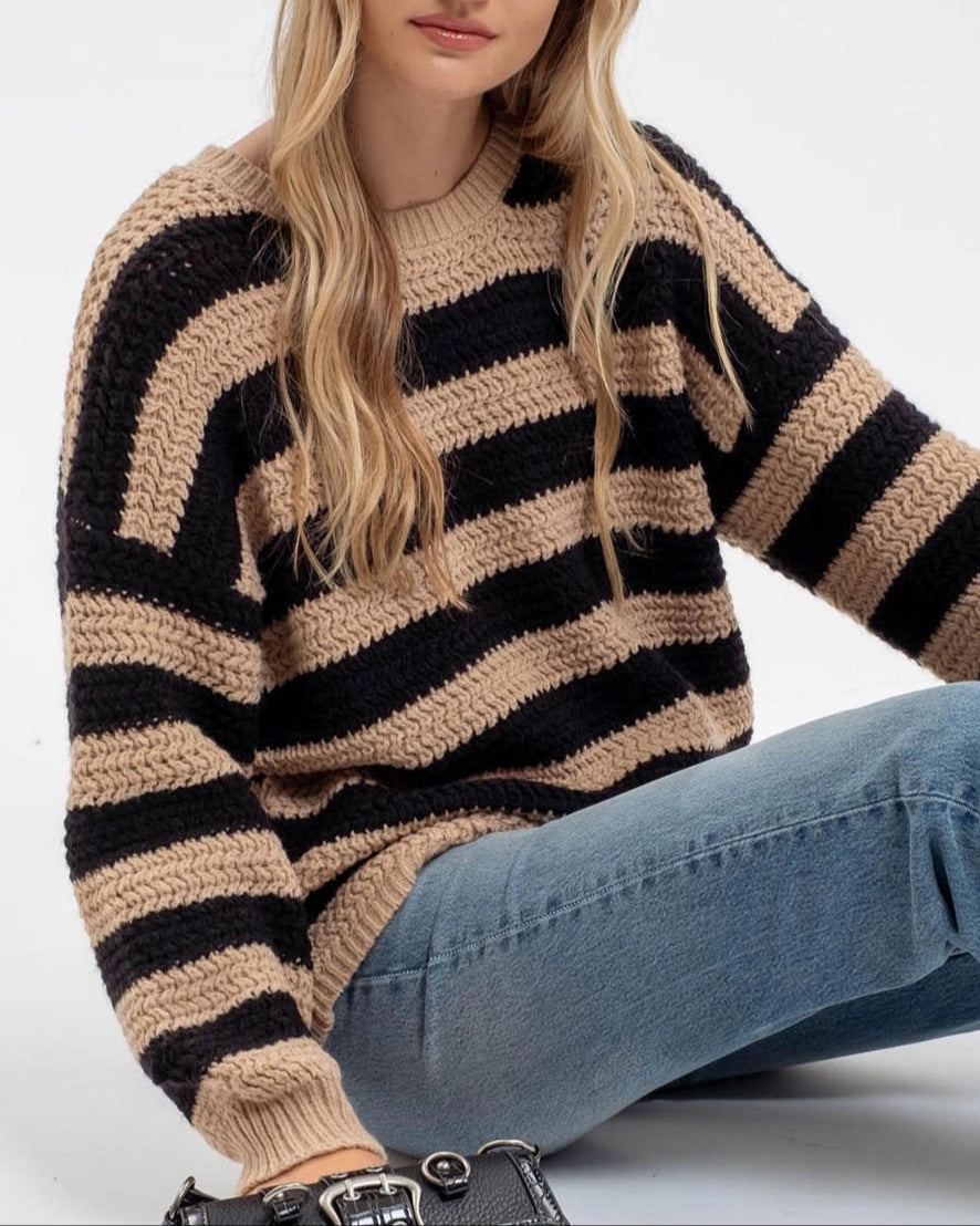 Woman wearing a black and beige striped sweater with blue jeans on a white background.