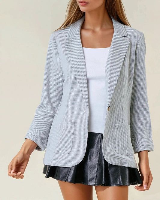Woman wearing a grey textured blazer over a white top and black skirt on a beige background.