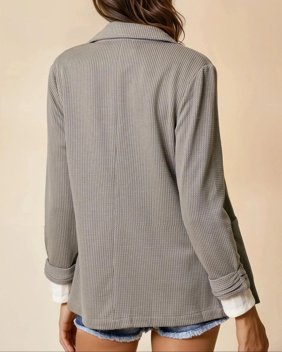 Woman wearing an Olive Textured blazer over a white shirt, and denim shorts on a beige background.