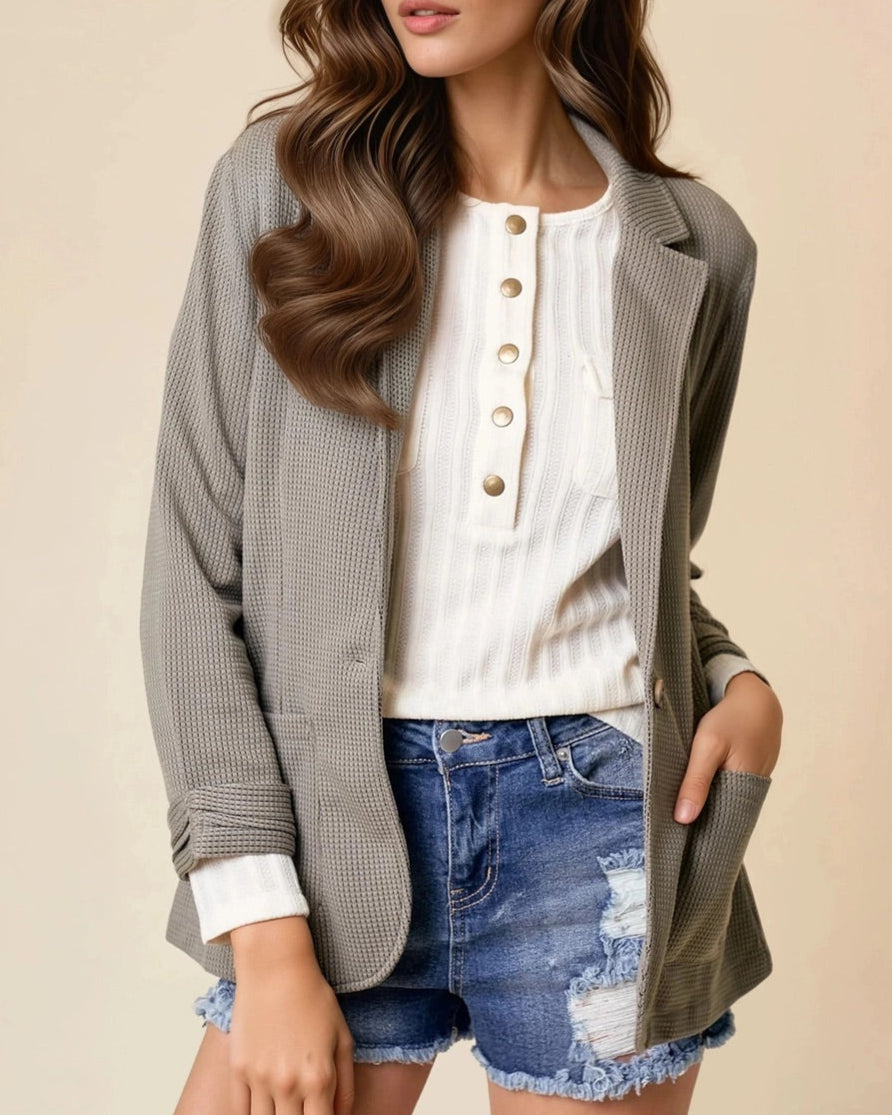 Woman wearing an Olive Textured blazer over a white shirt, and denim shorts on a beige background.