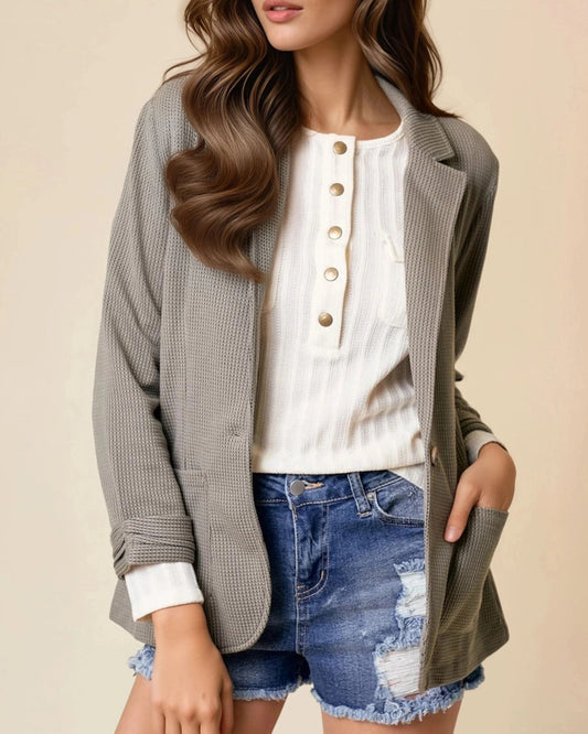Woman wearing an Olive Textured blazer over a white shirt, and denim shorts on a beige background.