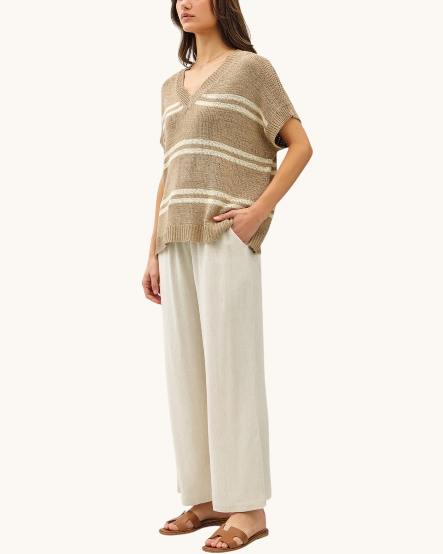 Woman wearing a taupe and white striped short sleeve sweater with wide-leg pants and brown sandals on a white background.