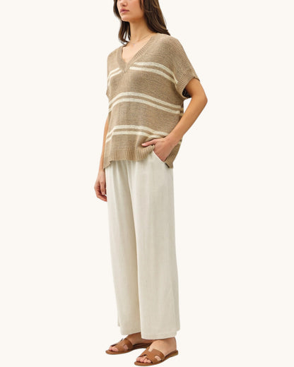 Woman wearing a taupe and white striped short sleeve sweater with wide-leg pants and brown sandals on a white background.
