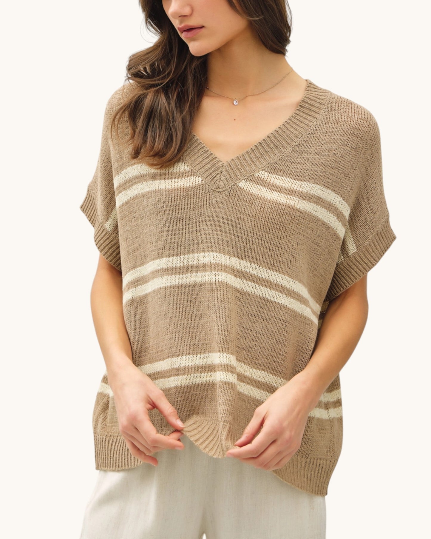 Woman wearing a taupe and white striped v-neck sweater on a white background.